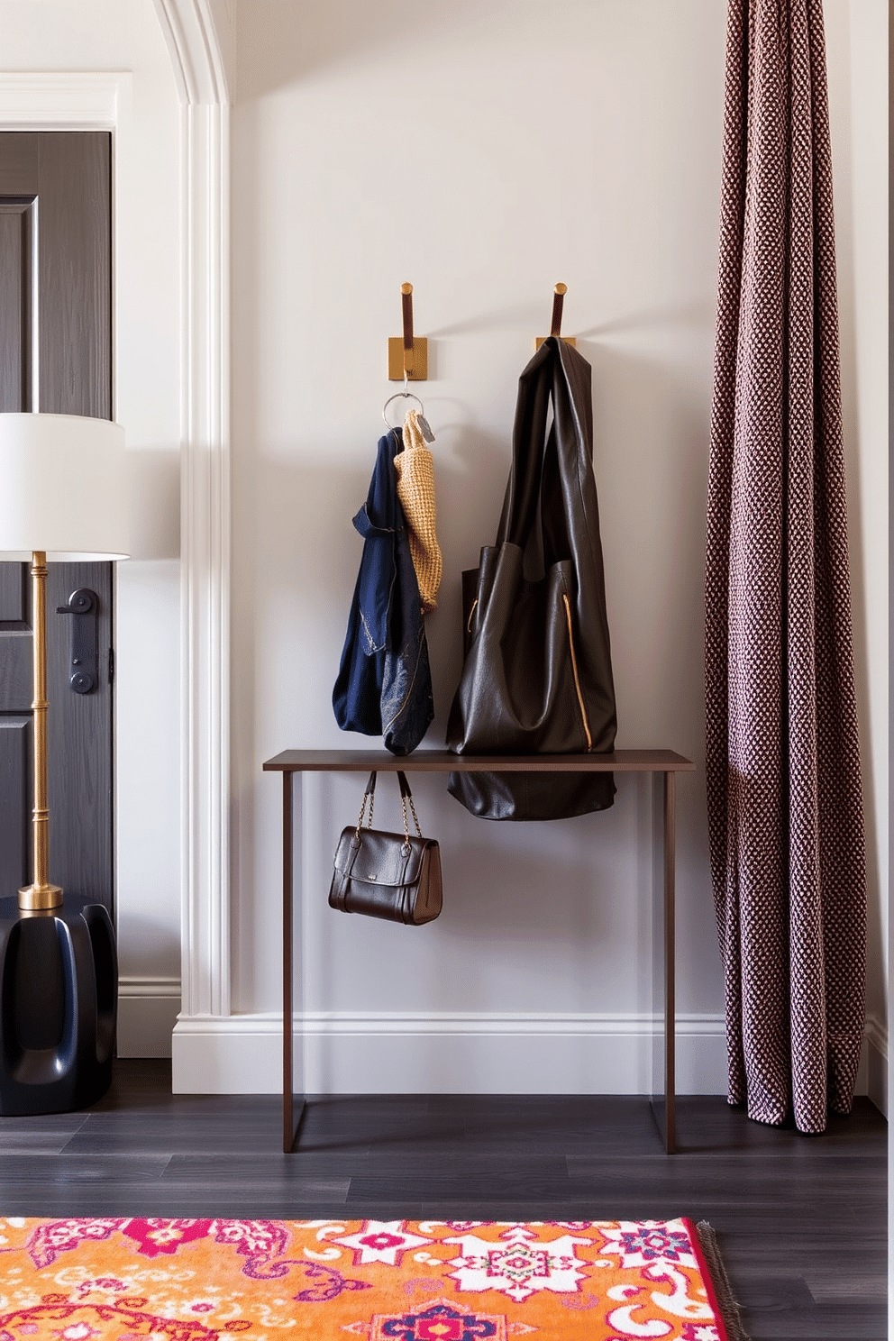 A stylish apartment entryway features a sleek console table against the wall, adorned with decorative hooks for keys and bags. The hooks are crafted from brushed brass, adding a touch of elegance, while a vibrant area rug in warm tones welcomes guests as they enter.