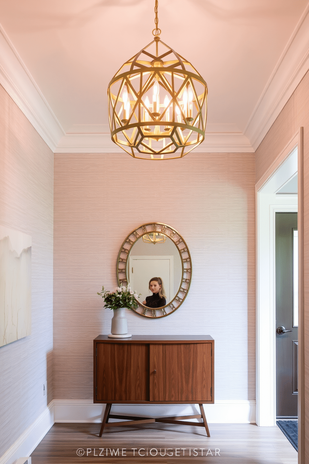 A unique light fixture hangs from the ceiling, casting a warm glow throughout the entryway. The fixture features an intricate design of geometric shapes in brushed brass, creating a striking focal point. The walls are adorned with a subtle textured wallpaper in soft gray tones, enhancing the welcoming atmosphere. A stylish console table with a rich walnut finish sits against the wall, complemented by a decorative mirror above it.