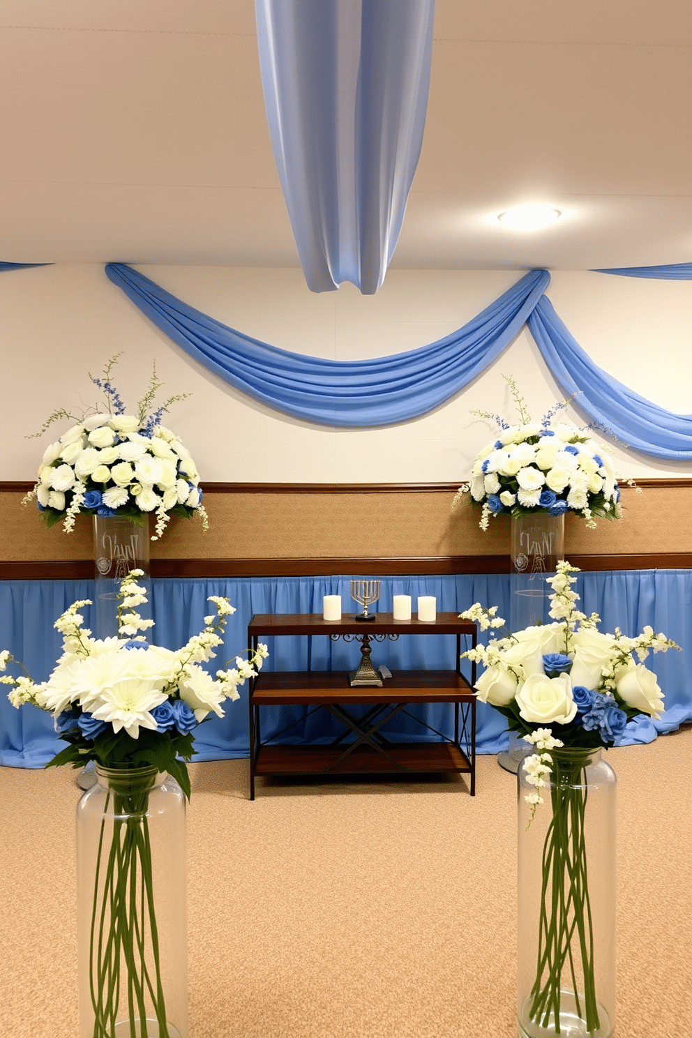 A serene basement space adorned for Hanukkah, featuring white and blue floral arrangements that beautifully complement the festive decor. The walls are draped with soft blue fabric, and a large menorah stands proudly on a wooden table surrounded by elegant white candles.