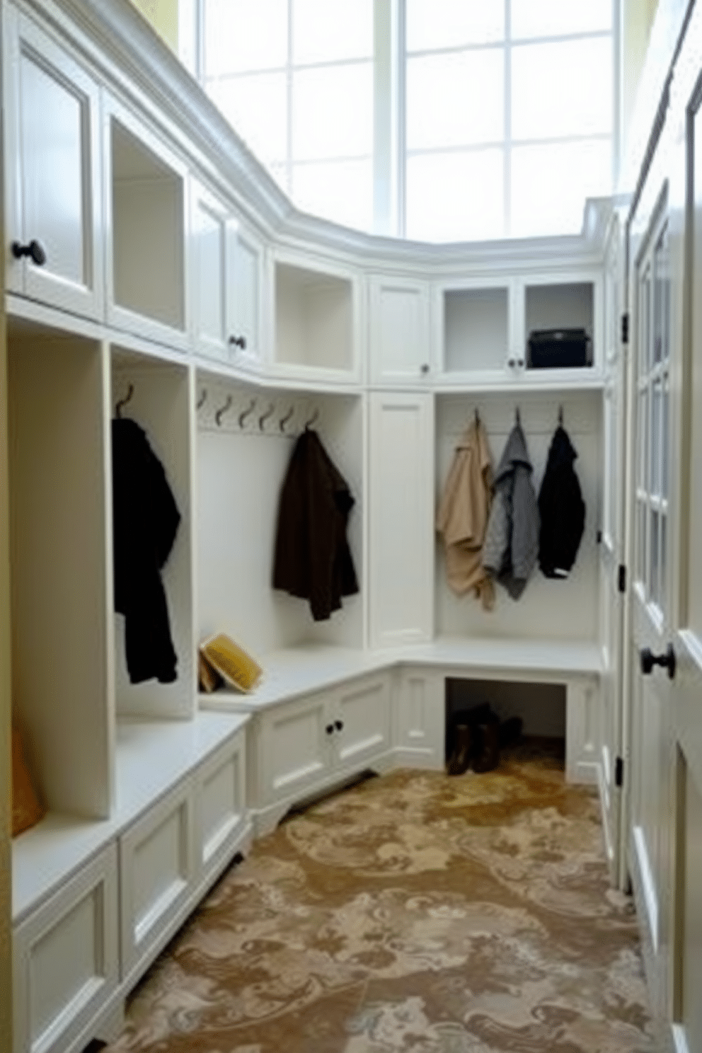 Classic white cabinetry for a clean look. The mudroom features built-in benches with plush cushions, and hooks for coats are mounted on the wall above. The flooring is a durable, patterned tile that contrasts with the cabinetry. Natural light floods the space through a large window, highlighting the organized storage solutions.