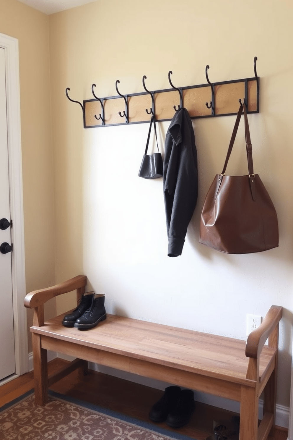 A rustic wood bench with a weathered finish sits against the wall, providing a cozy spot for sitting and removing shoes. Above the bench, a row of sturdy hooks made from wrought iron offers ample space for hanging coats and bags, creating an inviting entryway. The mudroom features a warm color palette, with soft beige walls that complement the natural wood tones of the bench. A durable, patterned rug lies beneath the bench, adding texture and warmth to the space while helping to catch dirt from shoes.