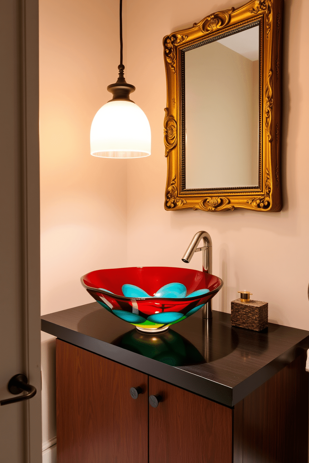 A striking powder room features a unique vessel sink crafted from hand-blown glass, showcasing vibrant colors that catch the eye. The sink is perched atop a sleek, dark wood vanity with modern hardware, creating a stunning contrast against the light-colored walls. The space is illuminated by a stylish pendant light that casts a warm glow, enhancing the room's inviting atmosphere. Complementing the design, a large framed mirror with an ornate gold frame hangs above the sink, reflecting the artistic details of the room.