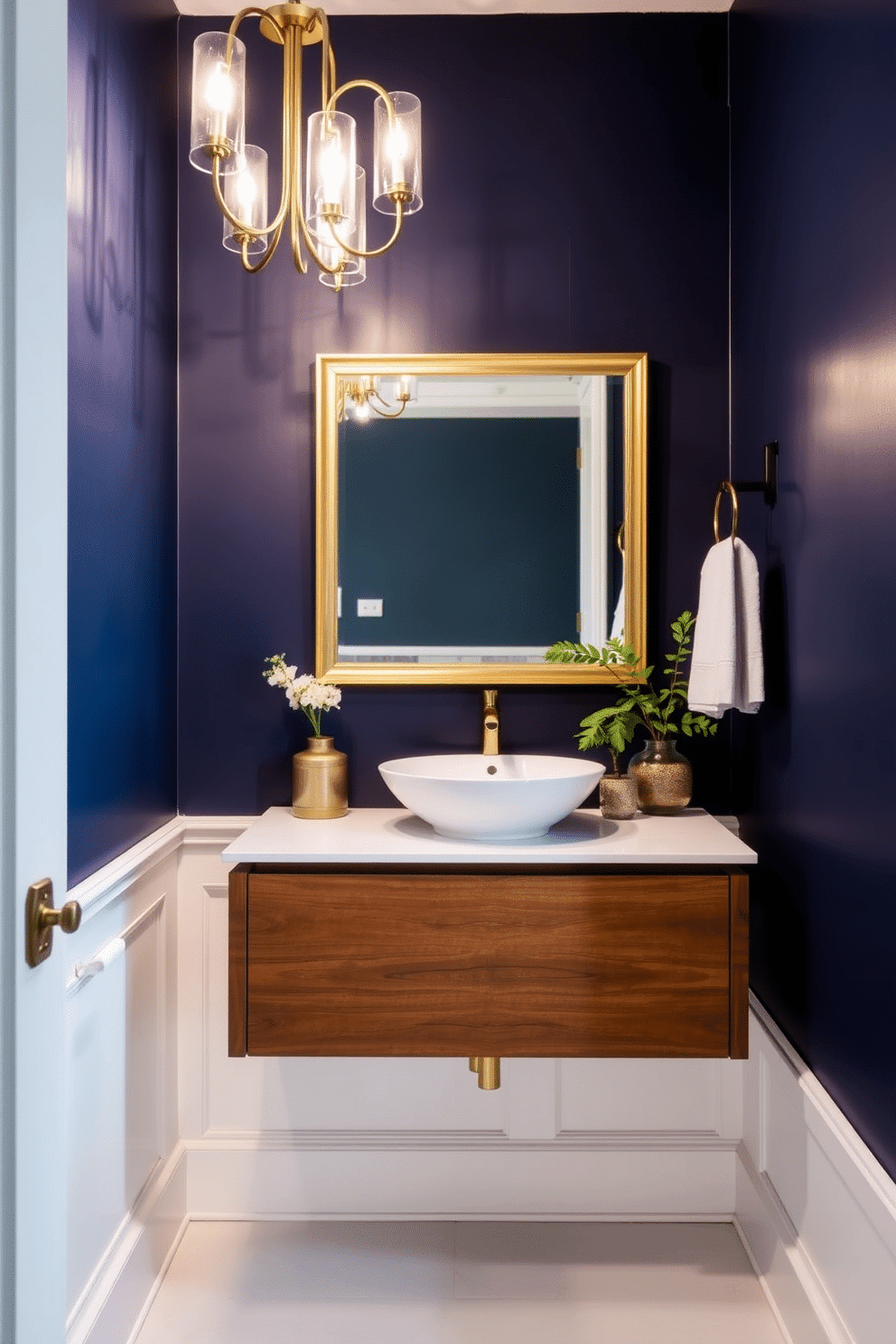 A bold accent wall in deep navy blue sets a dramatic backdrop for the powder room, creating a striking contrast with the crisp white wainscoting below. The space is illuminated by a modern chandelier, casting a warm glow that highlights the elegant fixtures and accessories. A sleek, floating vanity in a rich walnut finish complements the bold wall, topped with a white quartz countertop and a stylish vessel sink. Decorative elements, such as a gold-framed mirror and lush greenery, add a touch of sophistication and warmth to the overall design.