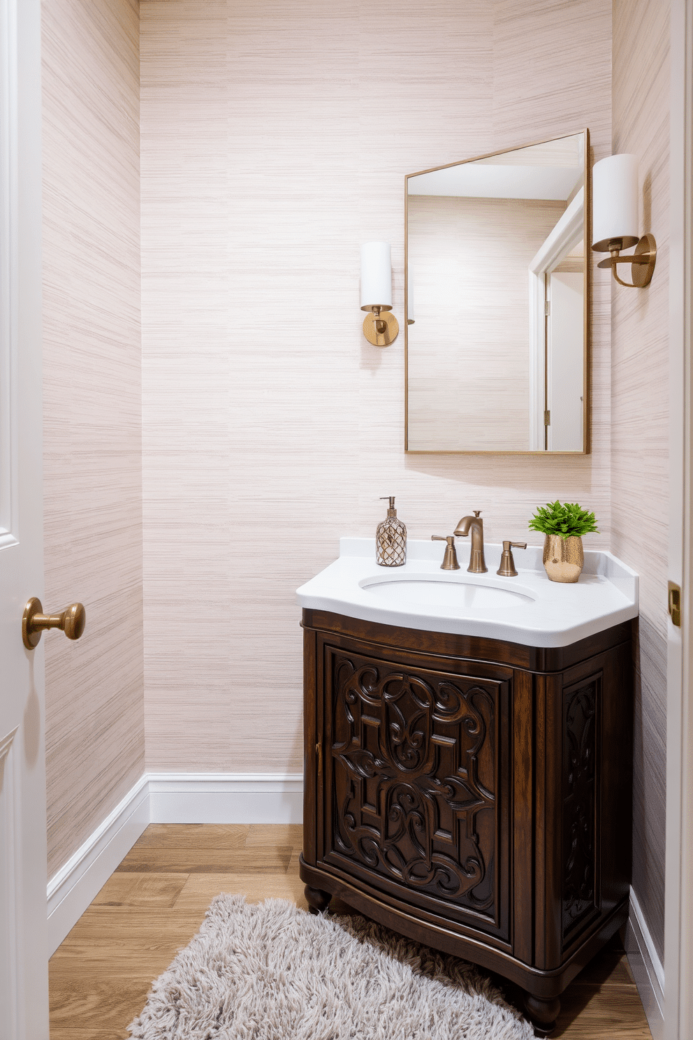 A stylish powder room featuring layered textures that create a warm and inviting atmosphere. The walls are adorned with a soft, textured wallpaper in a light taupe shade, complemented by a plush area rug in a deeper hue. The vanity showcases a rich wood finish with an intricate design, topped with a sleek white quartz countertop. Elegant accessories, including a decorative soap dispenser and a small potted plant, add a touch of sophistication to the space.