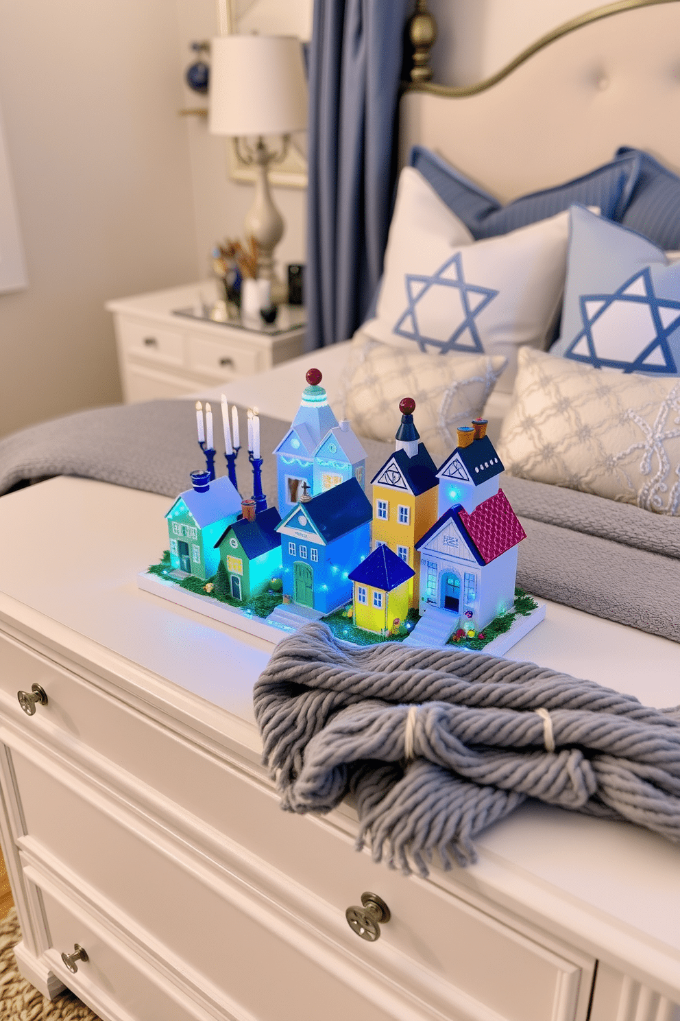 A charming miniature Hanukkah village is displayed on a dresser, featuring colorful houses adorned with blue and white lights. Each house is uniquely decorated with menorahs and dreidels, creating a festive atmosphere that captures the spirit of the holiday. The bedroom is elegantly decorated for Hanukkah, with soft blue and silver accents throughout. A cozy throw blanket is draped over the bed, while decorative pillows featuring Star of David motifs add a touch of seasonal cheer.