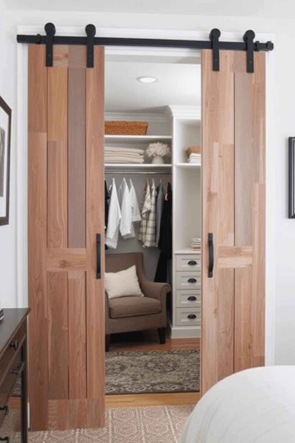 A charming bedroom walk-in closet featuring sliding barn doors made of reclaimed wood, adding a rustic touch to the space. Inside, custom shelving and hanging rods are organized efficiently, with a cozy armchair nestled in one corner for a stylish retreat.