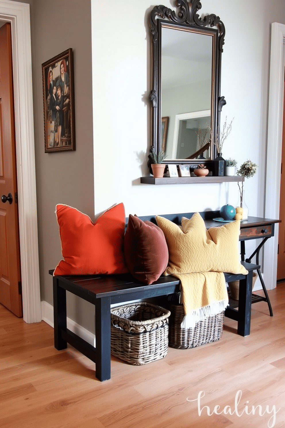 A rustic black wooden bench sits against the wall, adorned with plush, colorful cushions that invite comfort. The floor features natural wood planks, and a woven basket is placed underneath the bench for added storage. The foyer is designed with a warm, welcoming atmosphere, showcasing a mix of vintage and modern elements. A large mirror with an ornate frame hangs above a narrow console table, which is decorated with a few carefully selected plants and decorative items.