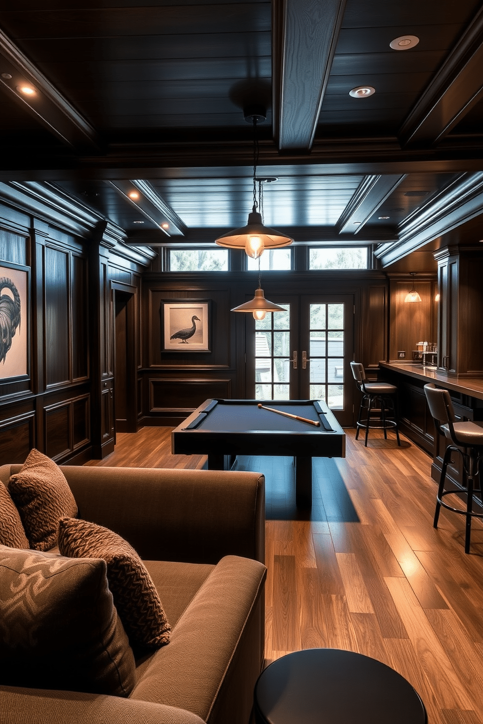 A cozy game room featuring dark wood accents throughout the space. The walls are adorned with rich, dark paneling, and a plush sectional sofa in deep gray invites relaxation. A sleek pool table takes center stage, surrounded by vintage-style pendant lighting that casts a warm glow. To one side, a custom-built bar with dark wood cabinetry offers a selection of drinks, complemented by high-backed stools for seating.