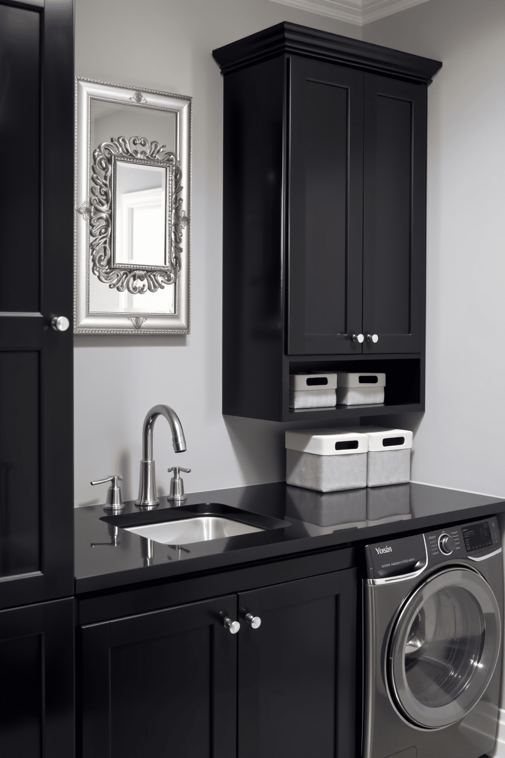 A modern laundry room featuring sleek black cabinetry with silver decorative accents. The space includes a stylish black countertop with a built-in sink, complemented by silver hardware and fixtures for a polished look. The walls are painted in a soft gray tone, enhancing the contrast with the black elements. A decorative silver-framed mirror hangs above the sink, while an organized shelf displays neatly folded towels and stylish storage bins.