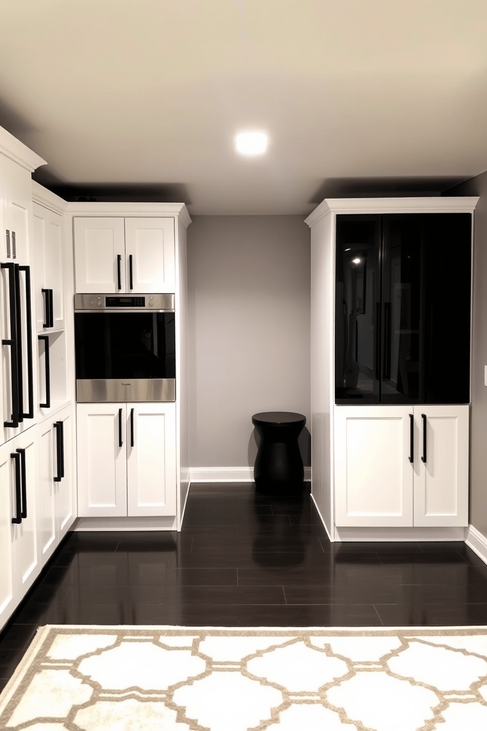 A modern basement design featuring white cabinetry with sleek black hardware accents. The space is illuminated by recessed lighting, highlighting the contrast between the cabinetry and the dark flooring. The walls are painted in a soft gray, creating a neutral backdrop for the bold black and white color scheme. A stylish rug with geometric patterns adds warmth and texture to the room, complementing the overall aesthetic.