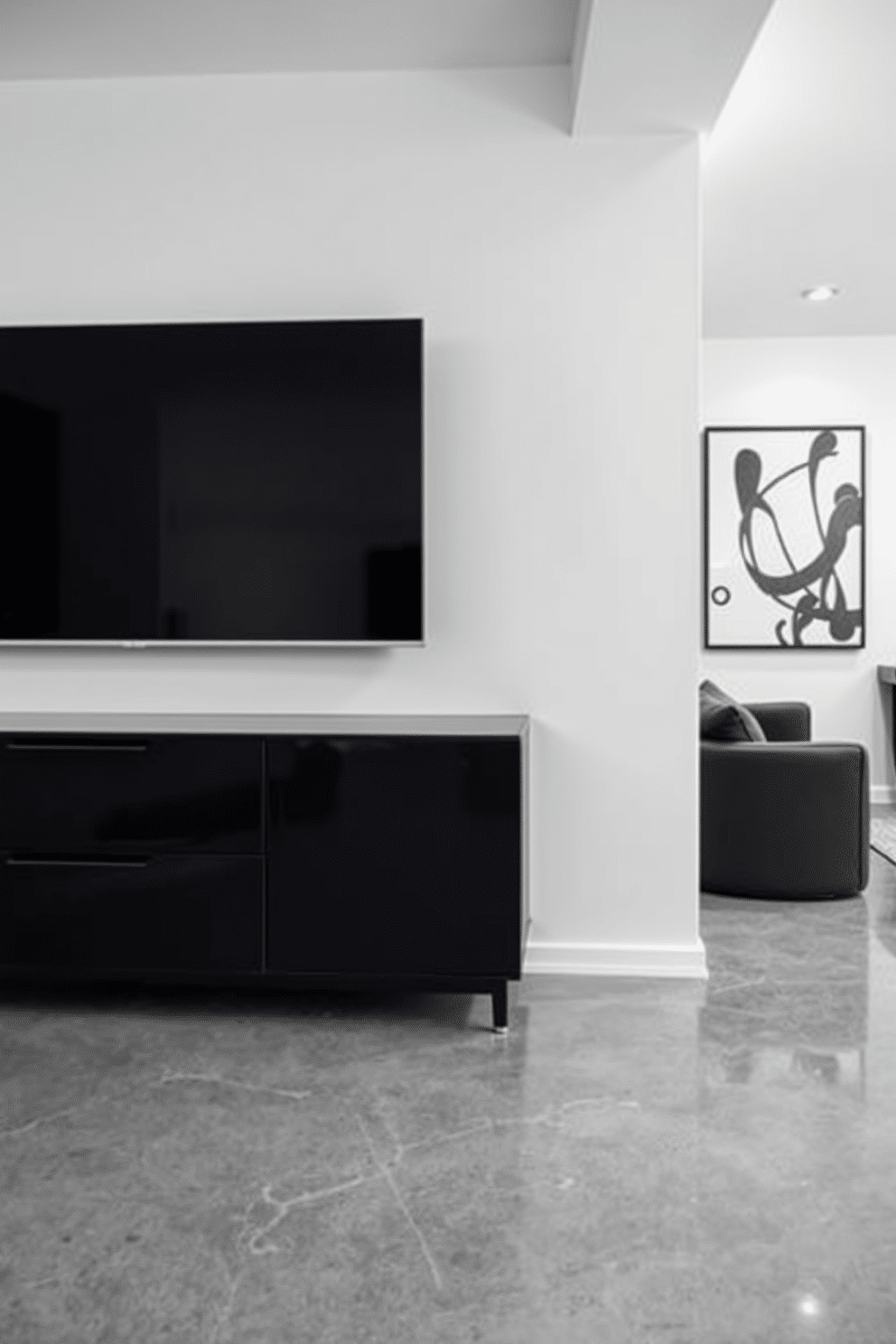 A sleek black media console is positioned against a crisp white wall, creating a striking contrast that enhances the modern aesthetic of the space. The console features clean lines and minimalist design, complemented by a large flat-screen TV mounted above it. In the basement, a black and white color scheme is employed to create a sophisticated and inviting atmosphere. The flooring consists of polished concrete, while the walls are adorned with abstract black and white art, adding a touch of elegance to the overall design.