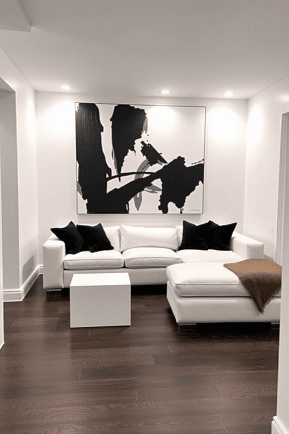 A stylish basement featuring a white sectional sofa adorned with black pillows as the focal point. The walls are painted in a crisp white, and the flooring is a sleek dark laminate, creating a striking contrast. In one corner, a minimalist coffee table complements the sofa, while a large abstract black and white artwork hangs above it. Soft ambient lighting from recessed fixtures enhances the modern aesthetic, making the space inviting and cozy.