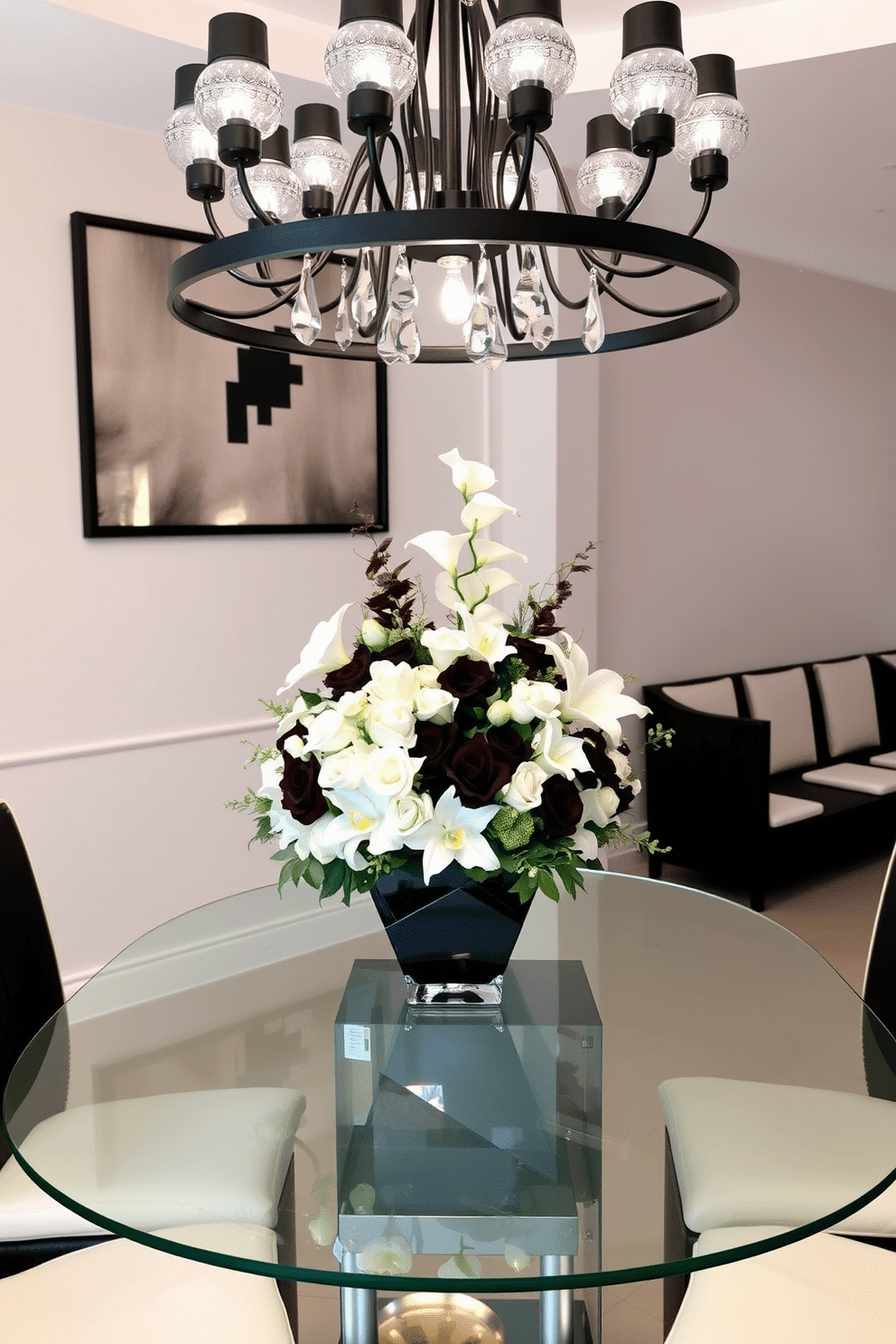 A stunning black and white floral centerpiece arrangement sits elegantly on a sleek glass dining table. The arrangement features an assortment of roses, lilies, and orchids, artfully arranged in a modern geometric vase. The dining room is designed with a monochromatic palette, featuring black chairs with white cushions around the table. A statement chandelier with black and white accents hangs above, casting a warm glow over the stylish setting.