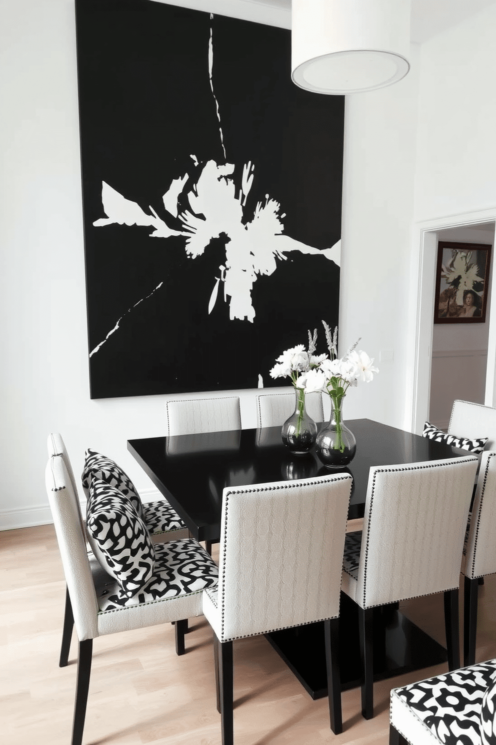 A stylish dining room featuring a sleek black table surrounded by chairs adorned with black and white patterned cushions. The walls are painted in a crisp white, and a bold black-and-white artwork hangs centrally, creating a striking focal point.