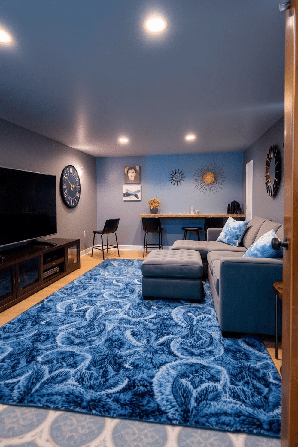 A cozy blue basement designed for relaxation. The space features a plush blue patterned area rug that adds texture and warmth, with a comfortable sectional sofa facing a sleek entertainment unit. Soft ambient lighting creates a welcoming atmosphere, while a small bar area with high stools invites casual gatherings. The walls are painted a soft gray, complemented by decorative art pieces that enhance the overall aesthetic.