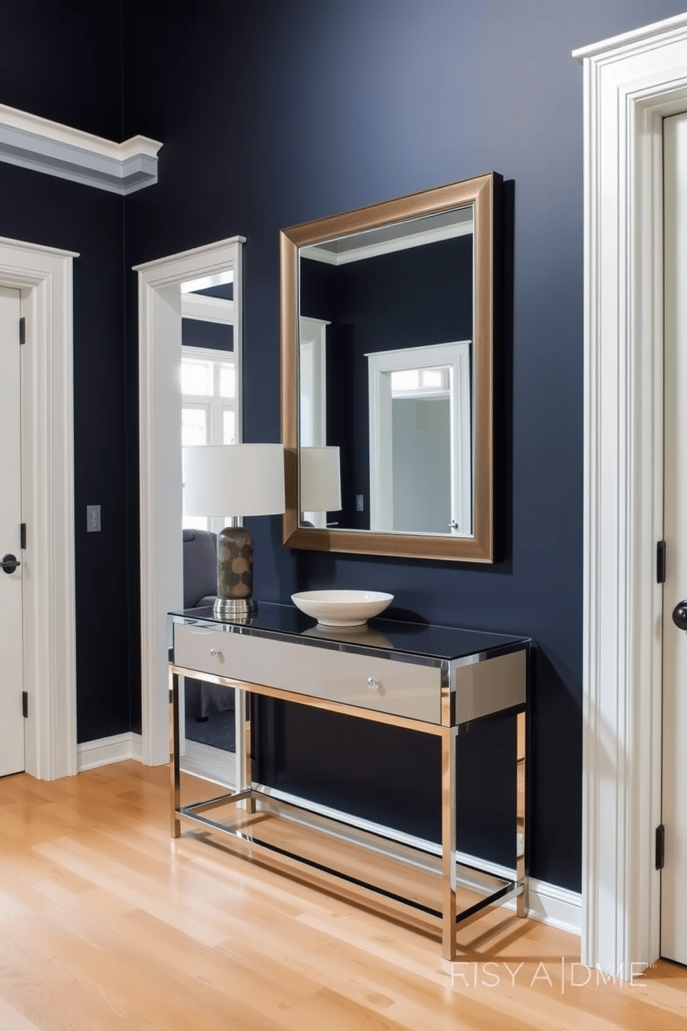 Elegant navy walls with white trim create a striking contrast that enhances the foyer's sophistication. A sleek console table with a glass top sits against the wall, adorned with a stylish lamp and a decorative bowl. The floor features a light-colored hardwood that complements the dark walls, adding warmth to the space. A large, framed mirror is hung above the console, reflecting natural light and making the area feel more spacious.