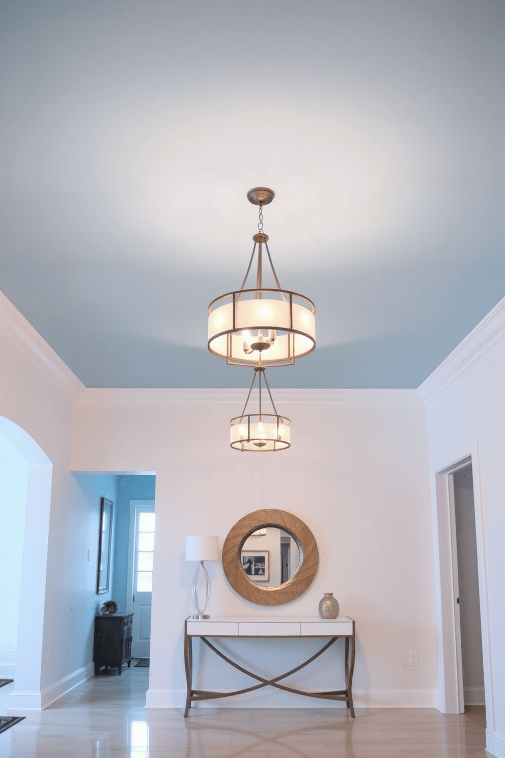 A serene foyer featuring a sky blue ceiling adorned with elegant pendant lighting that casts a warm glow. The walls are painted in a soft white, complemented by a stylish console table with a decorative mirror above it, creating an inviting atmosphere.