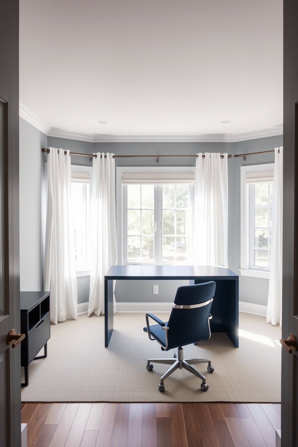 A serene home office designed in a muted blue and gray color palette. The walls are painted a soft gray, complemented by a deep blue accent wall behind a sleek, modern desk. The desk features a minimalist design with clean lines and is paired with an ergonomic chair in a matching blue hue. Natural light floods the space through large windows, adorned with sheer white curtains that enhance the tranquil atmosphere.