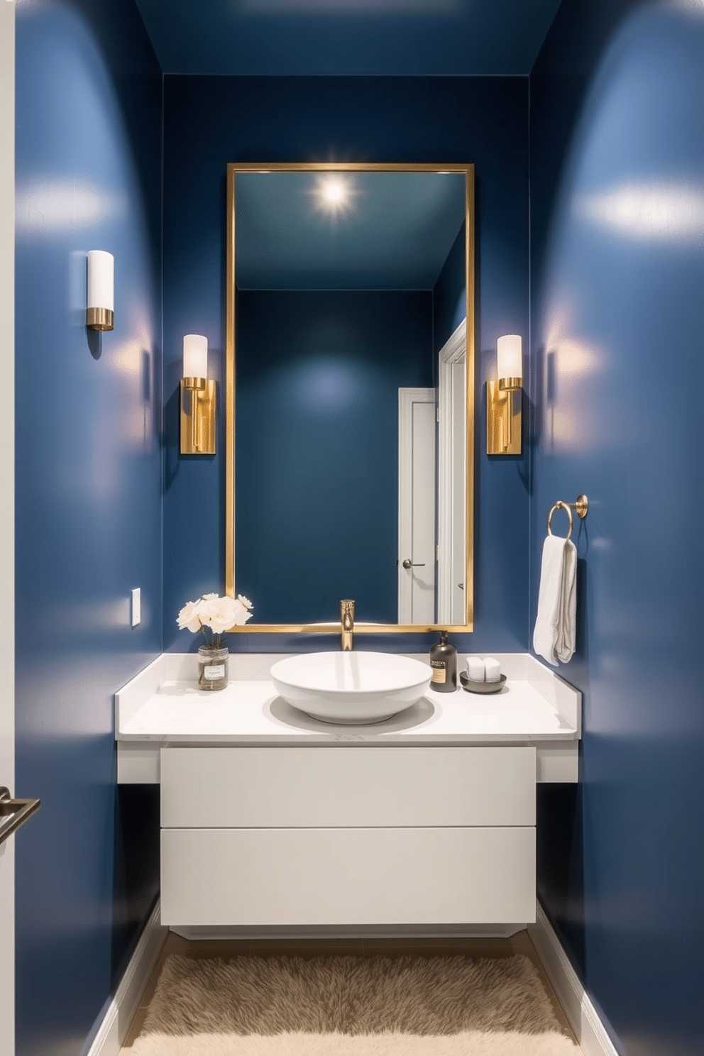 A chic powder room featuring rich blue walls that create a bold backdrop. Elegant gold sconces are mounted on either side of a large mirror, casting a warm glow throughout the space. The vanity boasts a sleek white countertop with a stylish vessel sink. A plush, patterned rug lies beneath, adding texture and comfort to the room.