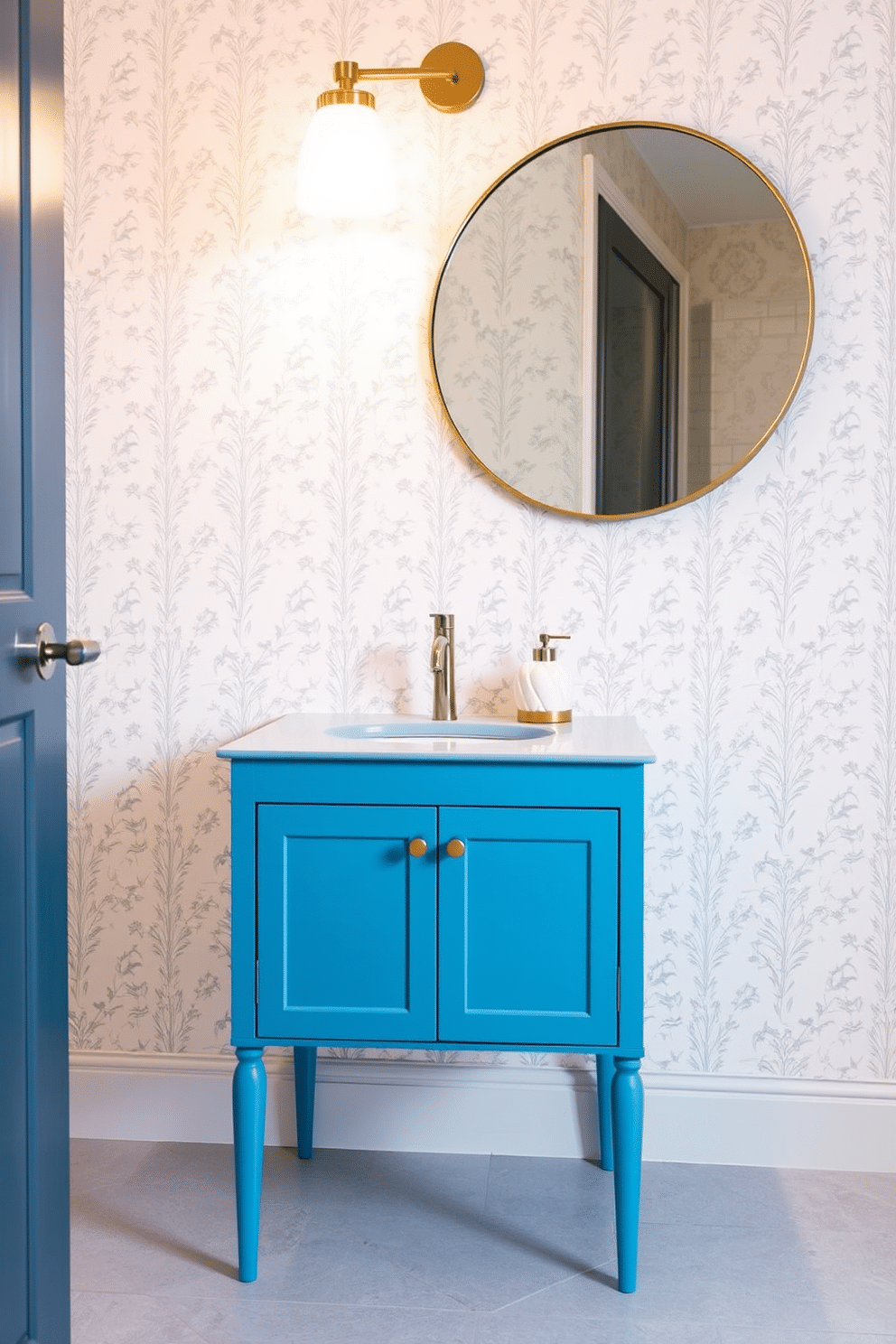 A compact blue vanity with a stylish faucet sits against a wall adorned with delicate wallpaper featuring a subtle floral pattern. The floor is covered in light gray tiles, while a round mirror with a sleek gold frame reflects the soft glow of a modern light fixture above.