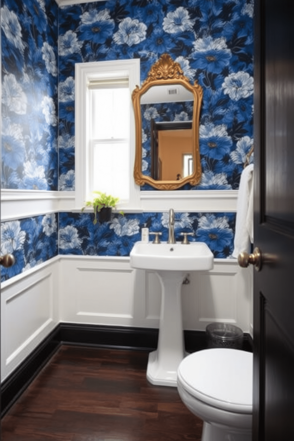 A chic powder room featuring bold blue floral wallpaper that creates a striking focal point. The space is accented with a sleek white pedestal sink and a vintage gold-framed mirror above it. The floor is adorned with dark wood tiles that contrast beautifully with the vibrant wallpaper. To enhance the elegance, a small potted plant sits on the windowsill, adding a touch of greenery to the design.