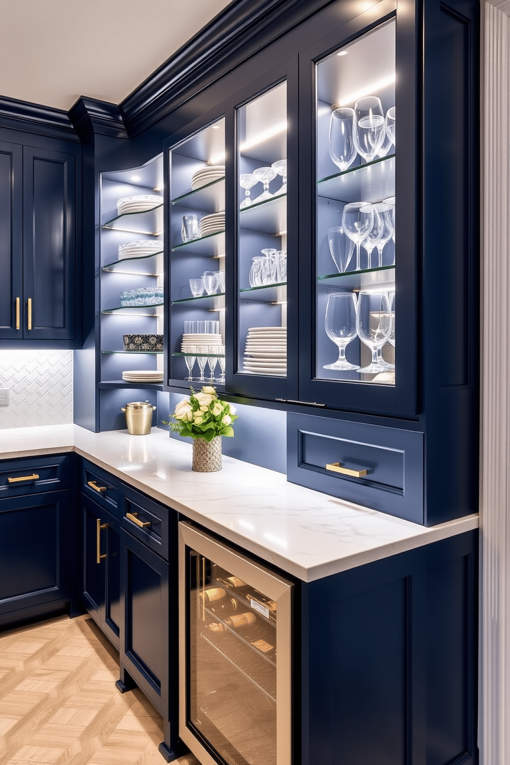 A stylish butler pantry featuring under-cabinet lighting that enhances the ambiance. The cabinetry is a rich navy blue with brass hardware, complemented by a white marble countertop and a herringbone tile backsplash. Soft, warm LED lights illuminate the shelves, showcasing elegant dishware and glassware. A small wine cooler is integrated into the design, providing a perfect space for entertaining guests.