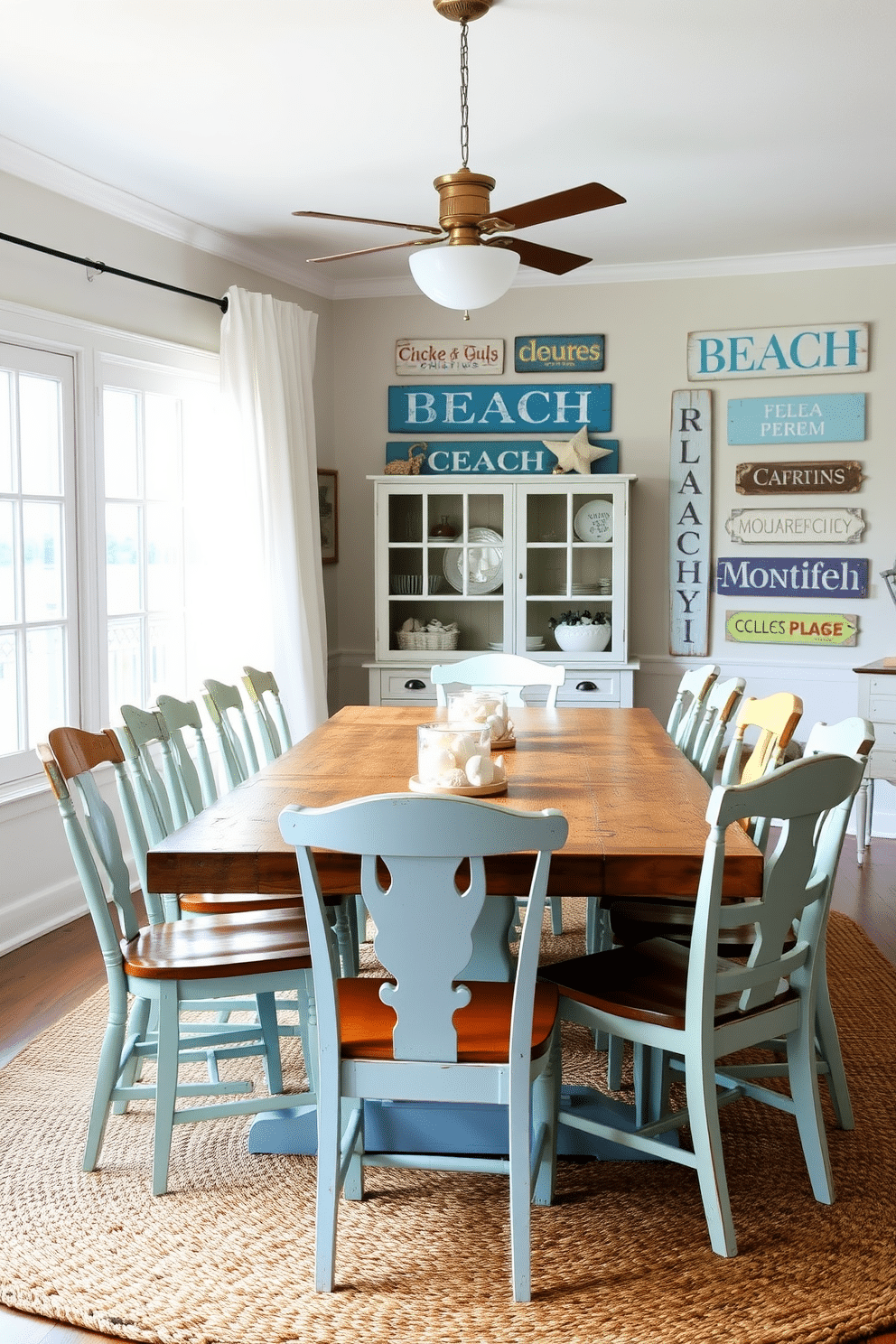 A coastal dining room features a large, rustic wooden table surrounded by mismatched chairs, each painted in soft pastel colors. Vintage beach signs adorn the walls, adding a playful touch and evoking a relaxed, seaside atmosphere. Natural light floods the space through large windows, with sheer white curtains gently billowing in the breeze. Nautical-themed decor, such as a woven jute rug and seashell centerpieces, enhances the coastal vibe while creating an inviting dining experience.