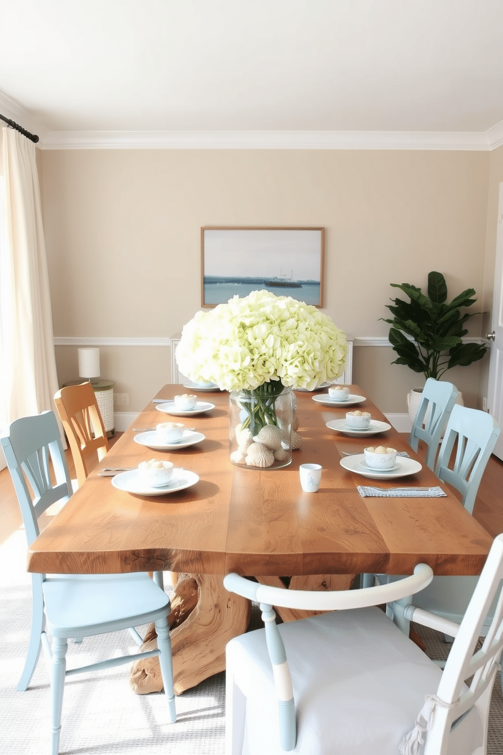 A coastal-themed dining room features a light, airy atmosphere with a large wooden table made from reclaimed driftwood. Surrounding the table are mismatched chairs in soft blues and whites, complemented by ocean-inspired tableware adorned with seashells and coral motifs. The centerpiece is a large glass vase filled with fresh white hydrangeas and sea glass accents. Natural light streams in through sheer linen curtains, illuminating a backdrop of soft sandy beige walls and a subtle nautical artwork.