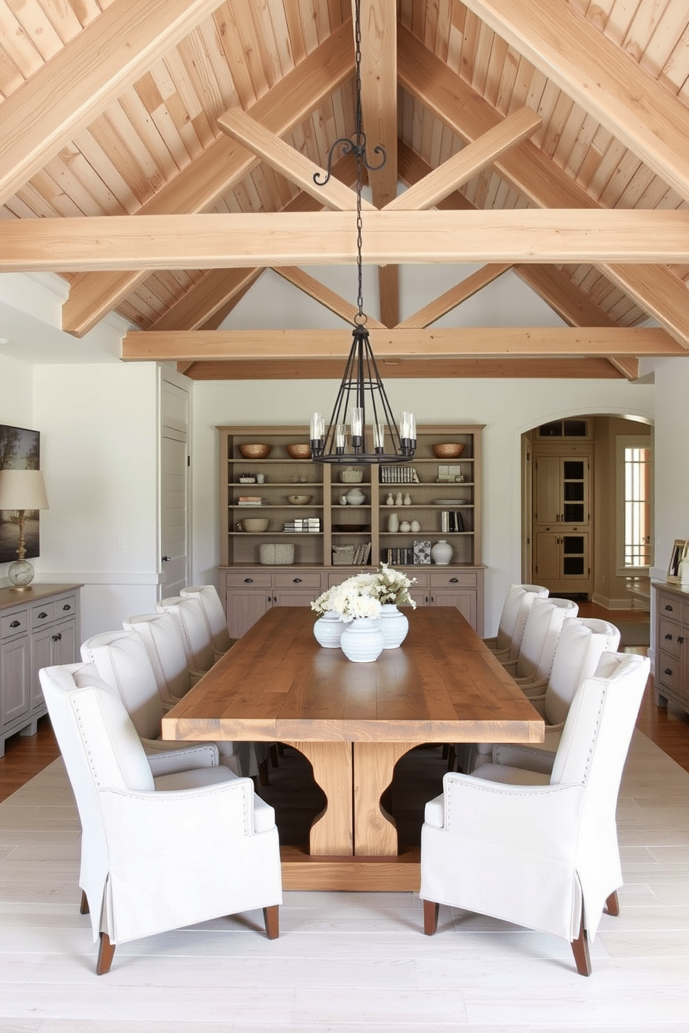 A coastal dining room featuring light wood beams that add architectural interest to the space. The room is adorned with a large, rustic dining table surrounded by comfortable, upholstered chairs in soft, neutral tones.