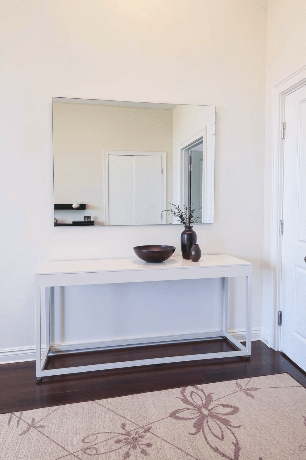 A minimalist console table is positioned against the wall in a condo entryway, featuring clean lines and a sleek finish. Above the table, a large, frameless mirror reflects the soft lighting, enhancing the sense of space and brightness. The floor is adorned with a subtle area rug that adds warmth without overwhelming the design. A few carefully selected decorative items, such as a small plant and a stylish bowl, are placed on the console to create an inviting atmosphere.