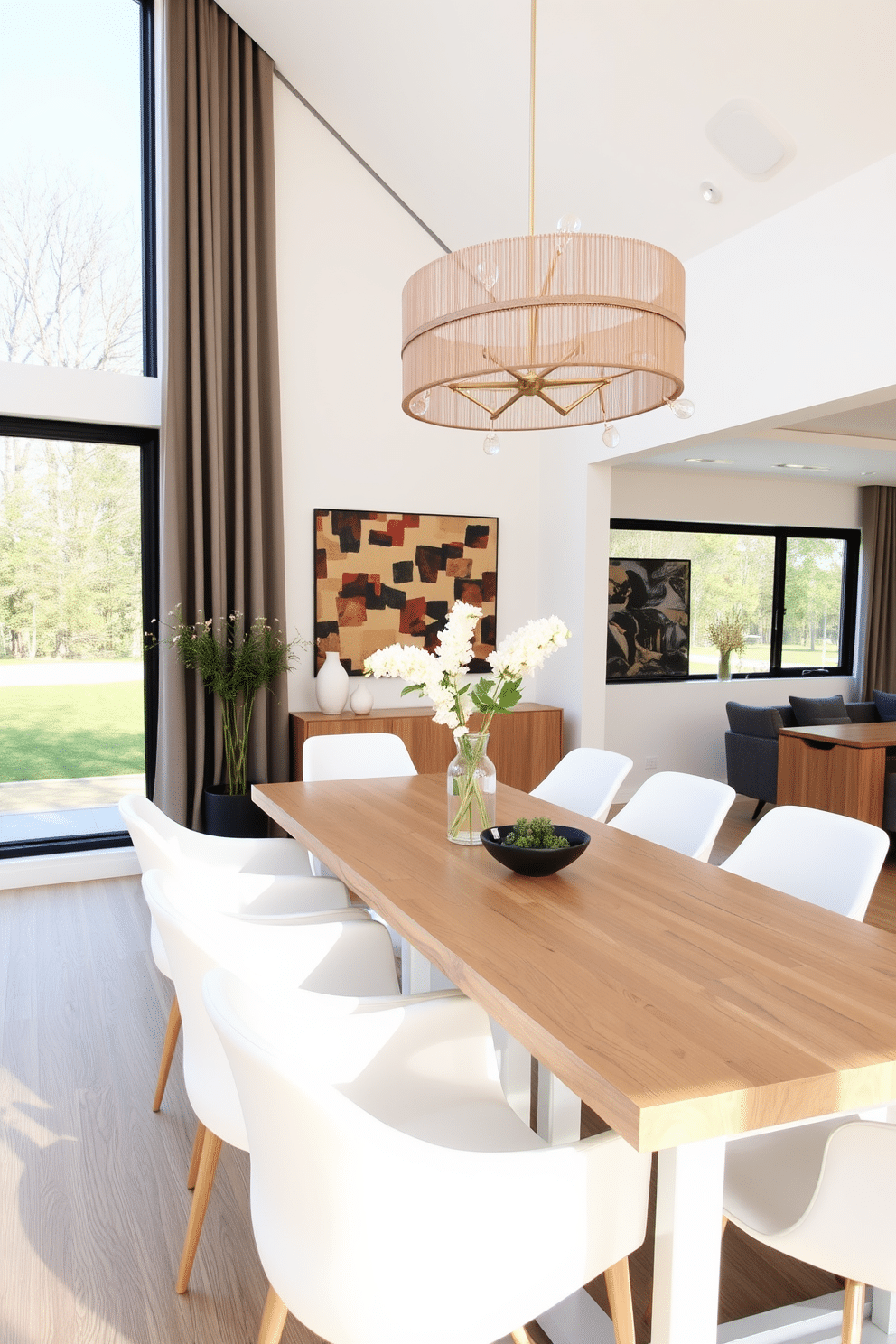 A contemporary dining room featuring a natural wood table surrounded by sleek white chairs. The space is illuminated by a modern chandelier overhead, with large windows allowing natural light to fill the room.