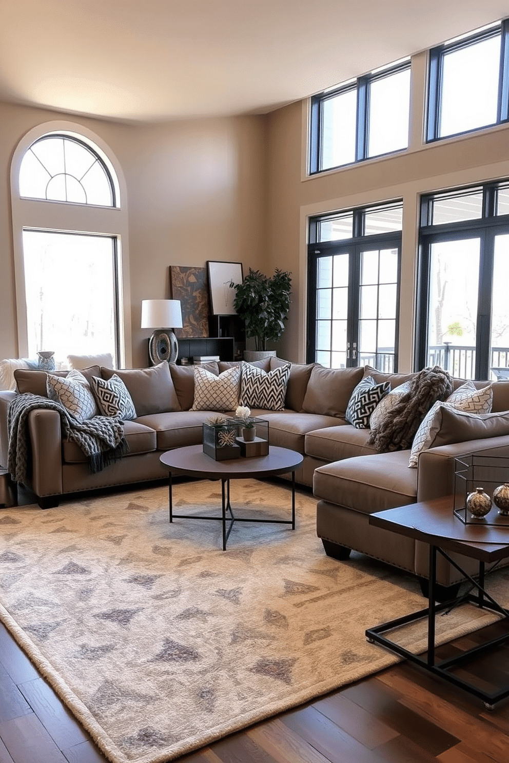 A contemporary family room featuring layered textures for visual interest. The space includes a plush sectional sofa adorned with a mix of patterned and solid throw pillows, complemented by a chunky knit throw draped over one arm. The walls are painted in a warm neutral tone, while a large area rug with geometric patterns anchors the seating area. Natural light floods in through floor-to-ceiling windows, highlighting a mix of wooden and metal accents throughout the room.