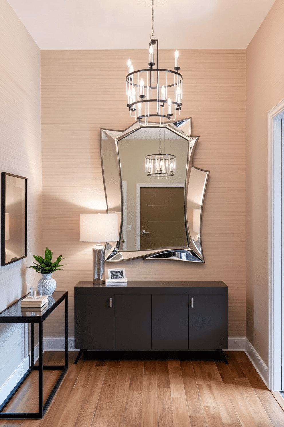 A contemporary foyer featuring a striking mirror with a unique, sculptural frame as the focal point. The space is illuminated by a modern chandelier, complementing the sleek lines of the furniture and the warm tones of the hardwood flooring. To the left, a minimalist console table holds decorative items and a small plant, adding a touch of greenery. The walls are adorned with subtle textured wallpaper, enhancing the overall sophistication of the entryway.