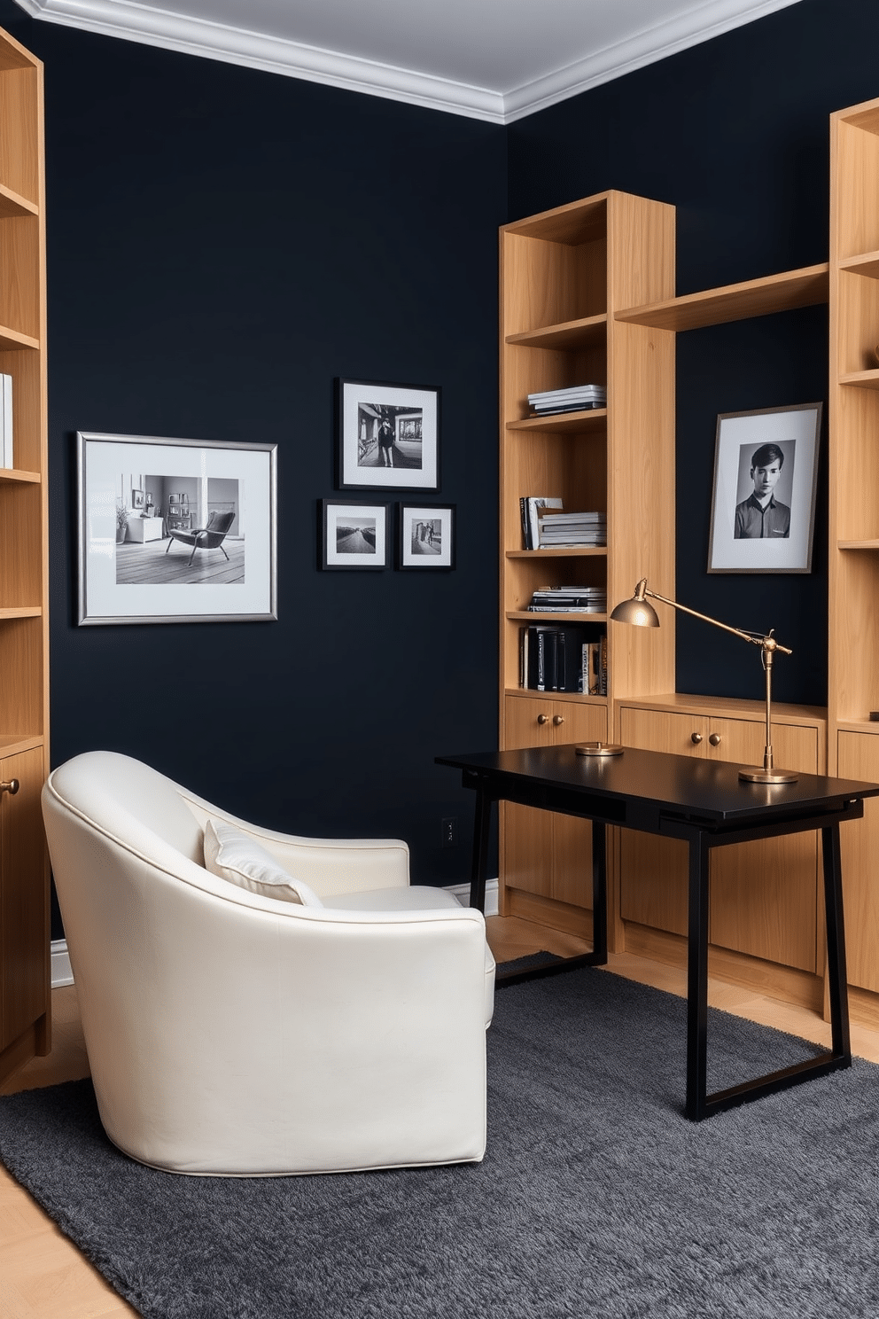 A cozy dark study room featuring deep navy blue walls contrasted by light oak shelving units. A large, plush cream-colored armchair sits in the corner, paired with a sleek black desk illuminated by a brass desk lamp. The floor is covered with a soft, dark gray area rug that adds warmth to the space. A collection of framed black-and-white photographs adorns the walls, creating a sophisticated gallery feel.