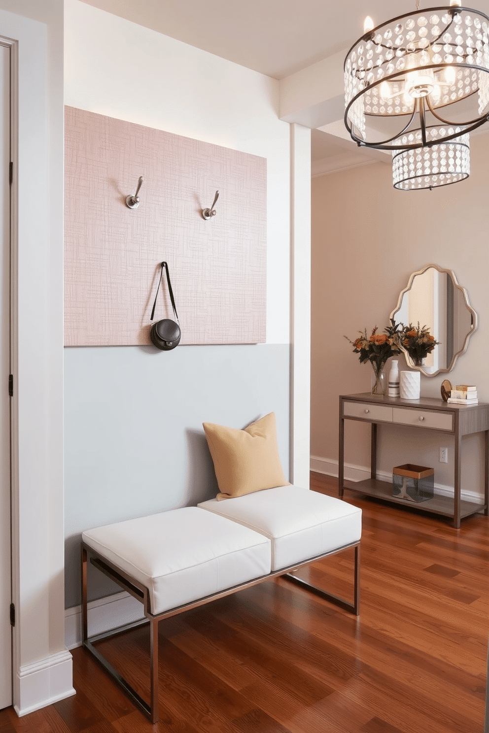 Chic coat hooks are mounted on a textured accent wall, adding a stylish touch to the entrance foyer. Below, a sleek bench with soft cushions invites guests to sit while removing their shoes, enhancing both functionality and comfort. The foyer features a statement light fixture that illuminates the space, casting a warm glow over the polished hardwood floor. A decorative console table against the wall showcases a curated selection of decorative items and a mirror, creating an inviting atmosphere.