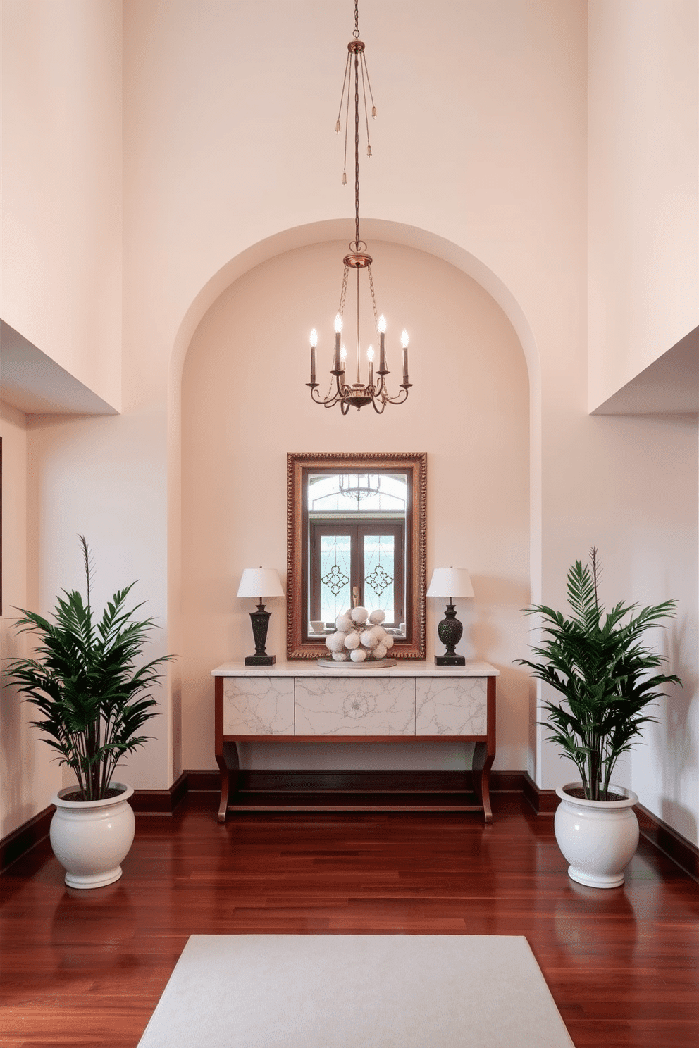 An elegant chandelier hangs from the high ceiling, casting a warm glow over the entrance foyer. The foyer features a grand console table with a marble top, adorned with decorative accents and a large mirror above it, reflecting the light beautifully. The walls are painted in a soft cream color, complemented by rich wooden flooring that adds warmth to the space. Flanking the entrance, tall potted plants bring a touch of greenery, enhancing the inviting atmosphere of the foyer.