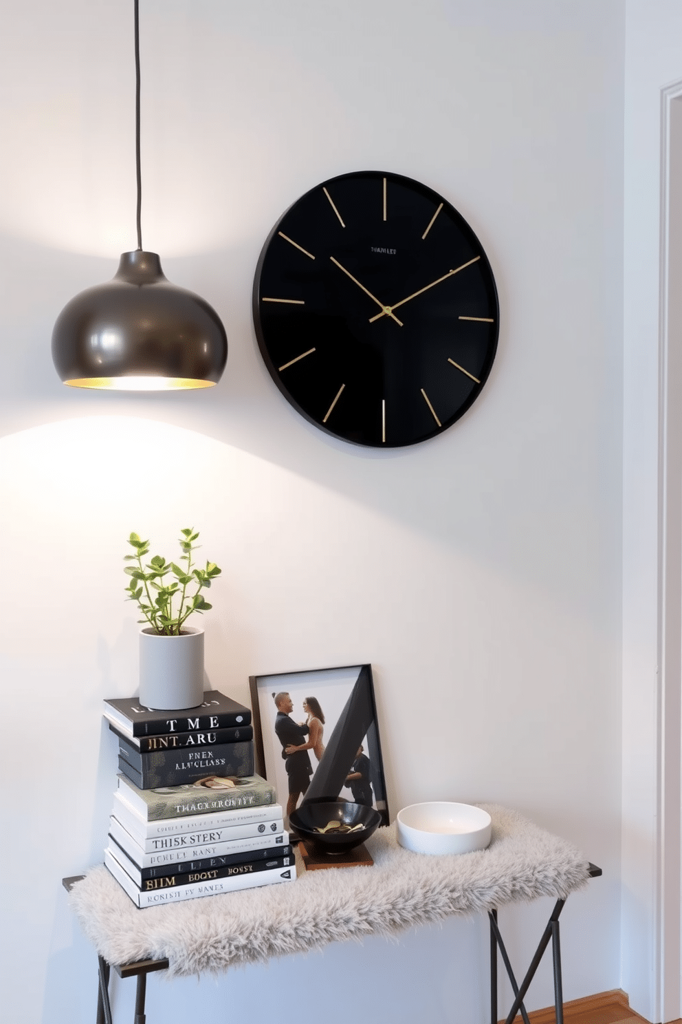 A chic clock with a sleek, minimalist design hangs on the wall, featuring a matte black finish and elegant gold hands. Below, a stylish entryway table showcases a mix of decorative elements, including a small potted plant, a stack of art books, and a decorative bowl for keys. The table is complemented by a plush, textured runner that adds warmth to the space. Soft lighting from a nearby pendant fixture casts a welcoming glow, enhancing the overall aesthetic of the entryway.