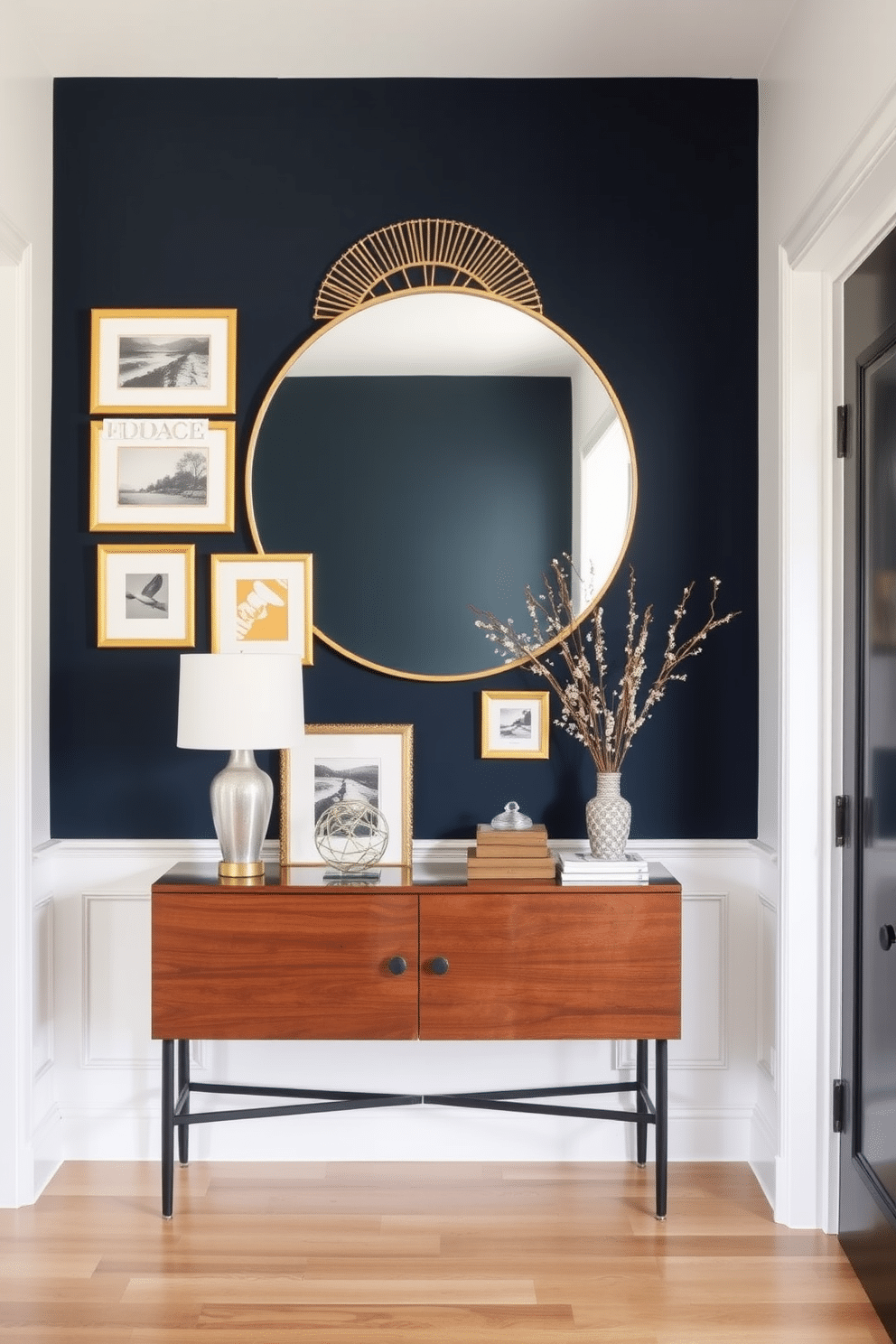 A bold accent wall painted in deep navy blue serves as the focal point of the entryway, creating a striking contrast against the soft white walls. A collection of framed art pieces in gold frames adorns the wall, adding a touch of elegance and personality to the space. In front of the accent wall, a sleek console table in a rich walnut finish showcases a stylish arrangement of decorative items. A large round mirror with a decorative gold border hangs above the table, reflecting light and enhancing the overall ambiance of the entryway.