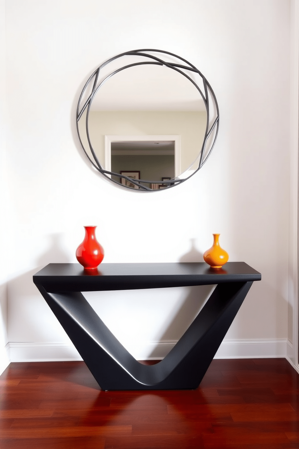 A sleek entryway table features a combination of modern geometric shapes, with a triangular base supporting a rectangular top. The table is finished in a matte black, creating a striking contrast against the light-colored walls and polished hardwood floor. Above the table, a round mirror with an asymmetrical frame adds depth and interest to the space. Flanking the table are two sculptural vases in bold colors, enhancing the contemporary vibe while providing a welcoming aesthetic.