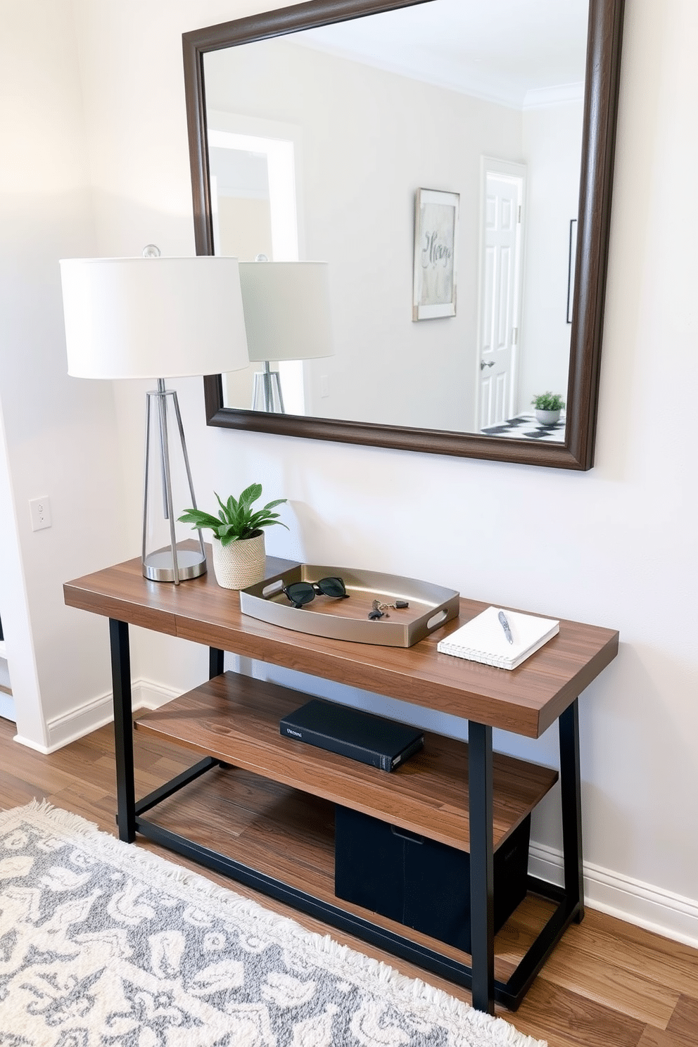 A stylish entryway table adorned with a decorative tray for keys and essentials. The table features a sleek wooden finish, complemented by a minimalist lamp and a small potted plant, creating an inviting atmosphere. The decorative tray is crafted from brushed metal, elegantly holding keys, sunglasses, and a notepad. Surrounding the table, a soft area rug adds warmth, while a large mirror above enhances the space and reflects light.