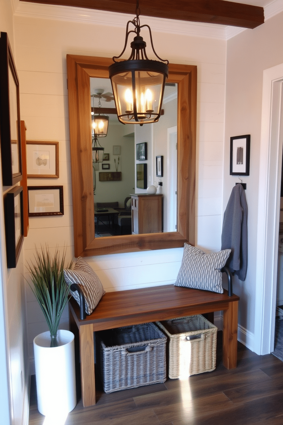 A warm and inviting entryway features rustic wood accents, including a reclaimed wood bench and a shiplap accent wall. Soft lighting from a wrought-iron chandelier casts a gentle glow, enhancing the cozy atmosphere. The walls are adorned with a mix of framed artwork and a large mirror with a distressed wooden frame, creating a welcoming focal point. A woven basket sits underneath the bench, providing storage for shoes and adding to the rustic charm.