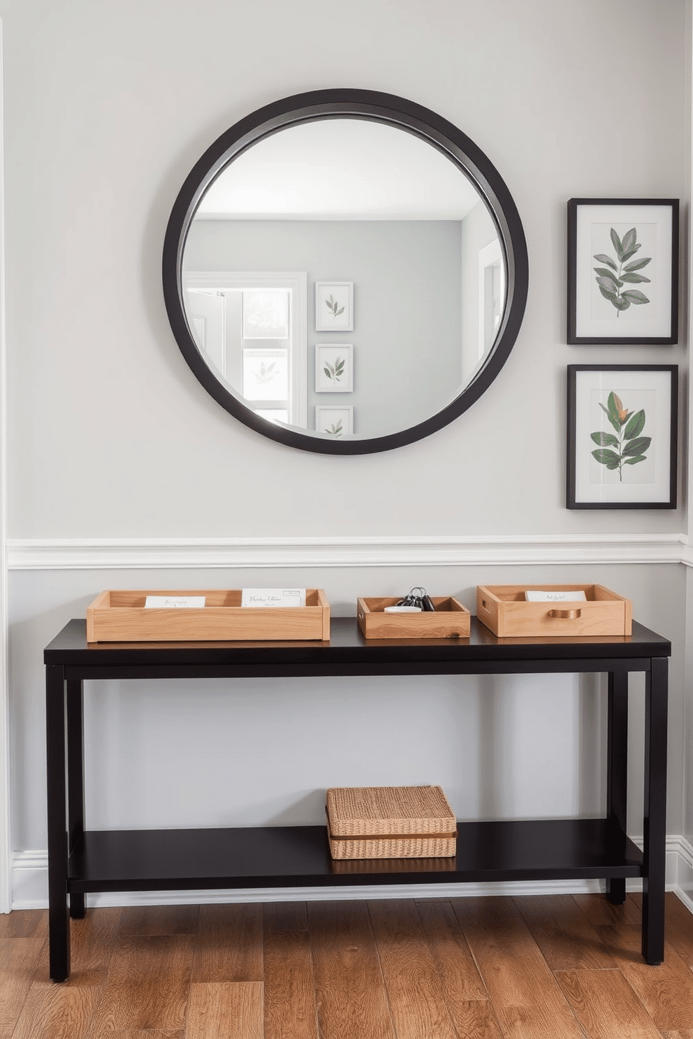 A stylish entryway features a modern console table adorned with decorative trays for keys and mail. The trays are crafted from natural wood and ceramic, adding texture and warmth to the space. The wall behind the console is painted in a soft gray hue, complemented by a series of framed botanical prints. A round mirror with a sleek black frame hangs above the table, reflecting the natural light that floods the entryway.