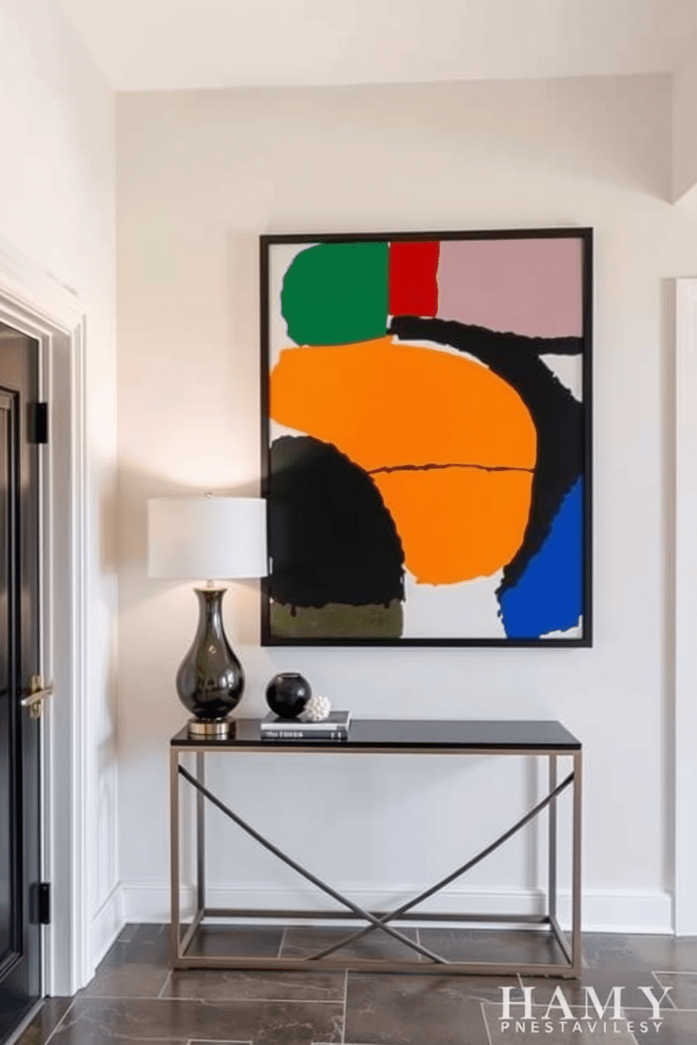 A striking entryway features a bold, large-scale artwork that commands attention, showcasing vibrant colors and abstract shapes. The artwork is framed in a sleek black frame, complementing the modern aesthetic of the space. The wall is painted in a soft, neutral tone to enhance the artwork's vibrancy, with a minimalist console table positioned below. A stylish lamp and a few curated decorative items adorn the table, creating an inviting atmosphere as guests enter the home.