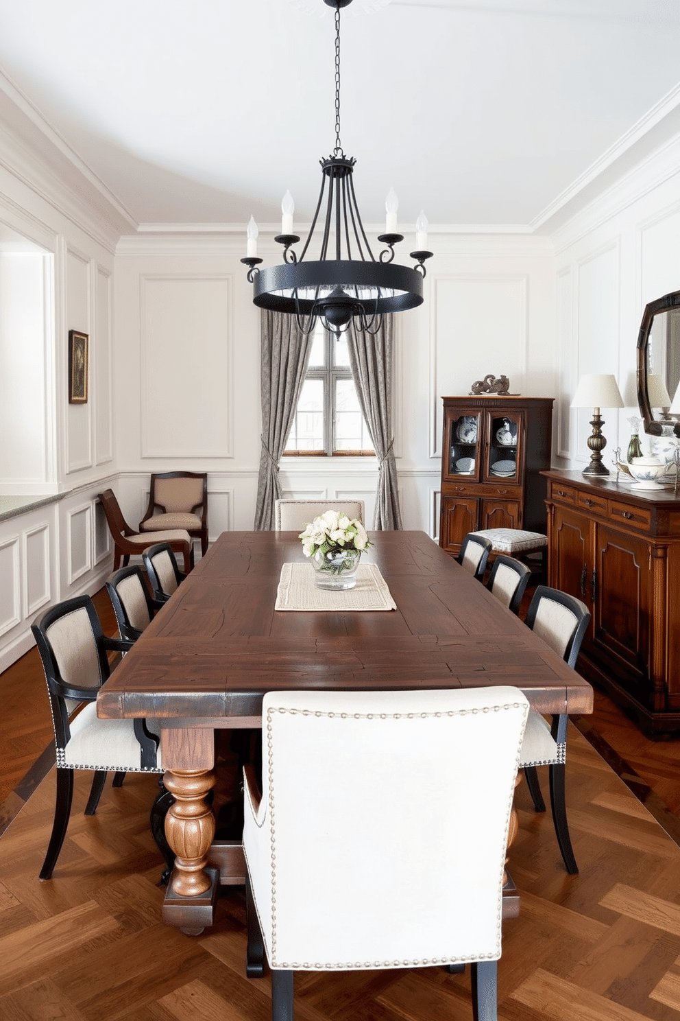 A European dining room that elegantly blends antique and modern furnishings. A large, rustic wooden table is surrounded by contemporary upholstered chairs, creating a striking contrast between old and new. The walls are adorned with classic wainscoting painted in a soft cream color, complemented by a modern chandelier that hangs gracefully above the table. A vintage sideboard, filled with decorative china, stands against one wall, adding character and warmth to the space.