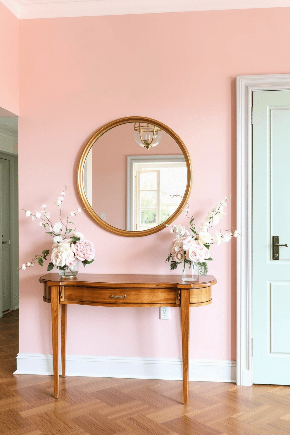 A serene European foyer adorned with soft pastel colors creates a calming atmosphere. The walls are painted in a delicate blush pink, complemented by a light mint green accent wall. A classic wooden console table is placed against the wall, topped with a large round mirror in a gold frame. Elegant floral arrangements in soft hues are displayed on the table, adding a touch of freshness to the space.