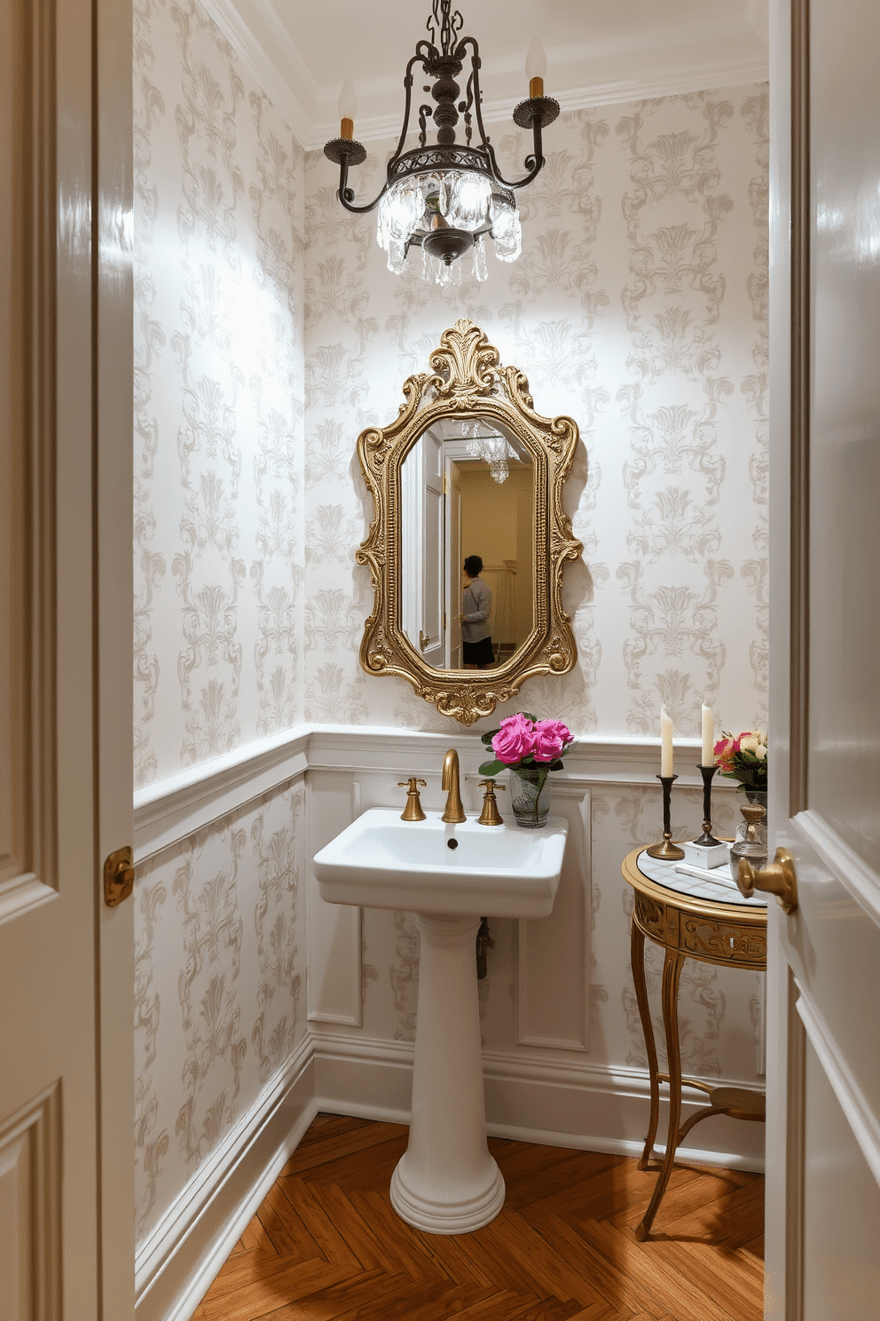 A charming European powder room features a blend of contemporary and vintage elements. The walls are adorned with elegant wallpaper in soft pastel tones, complemented by a sleek modern sink with a brushed brass faucet. A vintage-style mirror with intricate detailing hangs above the sink, reflecting the ambient lighting from a stylish chandelier. The flooring consists of classic herringbone wood, while a small antique side table holds fresh flowers and scented candles for a warm touch.