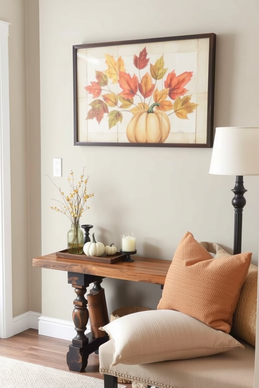 A warm and inviting entryway features seasonal artwork displayed prominently on the wall. The artwork showcases autumn leaves and pumpkins, bringing a cozy fall ambiance to the space. A rustic wooden console table sits beneath the artwork, adorned with small decorative gourds and a scented candle. Soft, textured throw pillows in warm tones are placed on a nearby bench, inviting guests to linger.