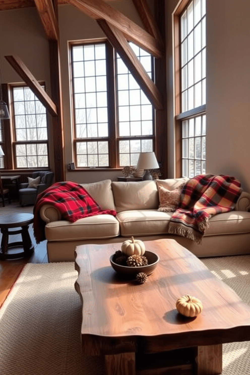 A cozy loft living room featuring a plush sofa adorned with warm plaid throws in shades of red, orange, and cream. Large windows allow natural light to flood the space, highlighting rustic wooden beams and a stylish coffee table made of reclaimed wood. The walls are painted in a soft beige, complementing the rich colors of the throws. A few carefully placed autumn-themed decorations, like small pumpkins and pinecones, add to the seasonal charm of the space.