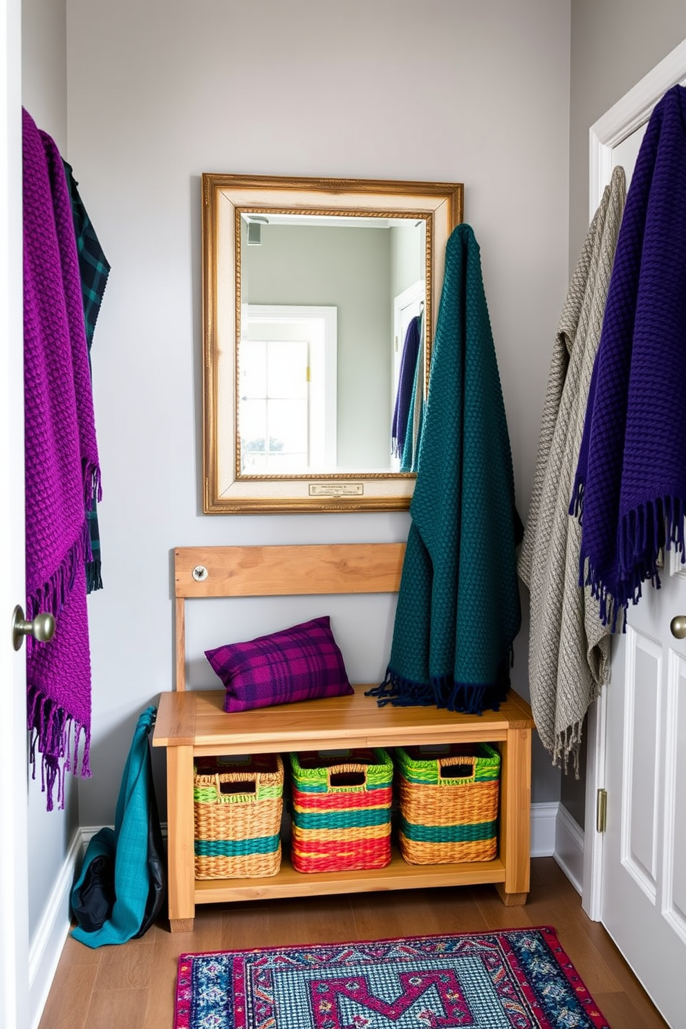 A cozy mudroom adorned with textured throws in rich jewel tones creates a welcoming atmosphere. The walls are painted in a soft gray, while a rustic wooden bench provides a perfect spot for removing shoes. Colorful woven baskets are neatly arranged under the bench, adding both functionality and style. A large mirror with a vintage frame hangs above a narrow console table, reflecting the vibrant hues of the throws.