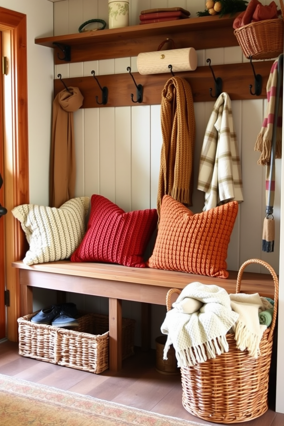 A cozy mudroom filled with warmth and charm. There are several soft knitted pillows in rich autumn colors placed on a wooden bench, inviting relaxation after outdoor activities. The walls are adorned with rustic hooks for hanging jackets and scarves. A woven basket sits nearby, filled with cozy blankets for chilly fall days.